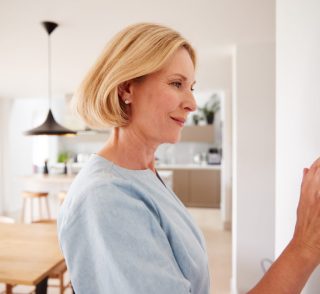Close Up Of Mature Woman Adjusting Central Heating Temperature At Home On Thermostat Close Up Of Mature Woman Adjusting Central Heating Temperature At Home On Thermostat
