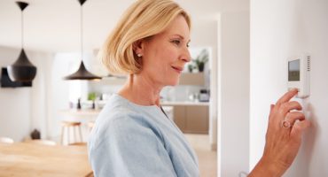 Close Up Of Mature Woman Adjusting Central Heating Temperature At Home On Thermostat